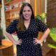 Tati Machado sorrindo, vestido preto de bolinhas brancas, mãos na cintura.