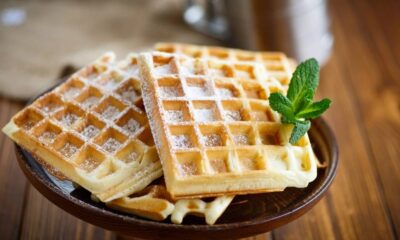 Três waffles dourados com açúcar de confeiteiro e um ramo de hortelã em prato de madeira