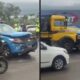 Caminhão amarelo colidiu com viatura policial azul danificada. Cena de acidente em rua molhada, com pessoas