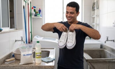 Homem sorridente segura tênis brancos em lavanderia; na bancada, sal grosso e vinagre.