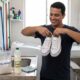 Homem sorridente segura tênis brancos em lavanderia; na bancada, sal grosso e vinagre.