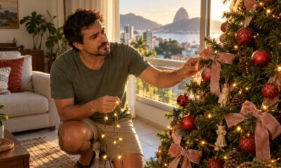 Árvore de Natal colada à janela recebe sol da tarde, e enfeites desbotam enquanto o pisca-pisca esquenta