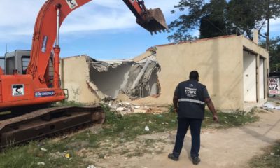 Imagem de uma retroescavadeira demolindo um casa