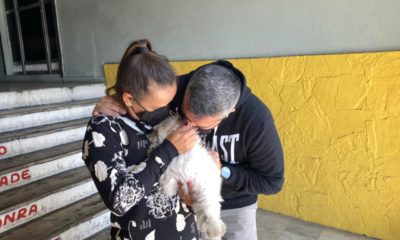 Cachorro sendo abraçado por duas pessoas