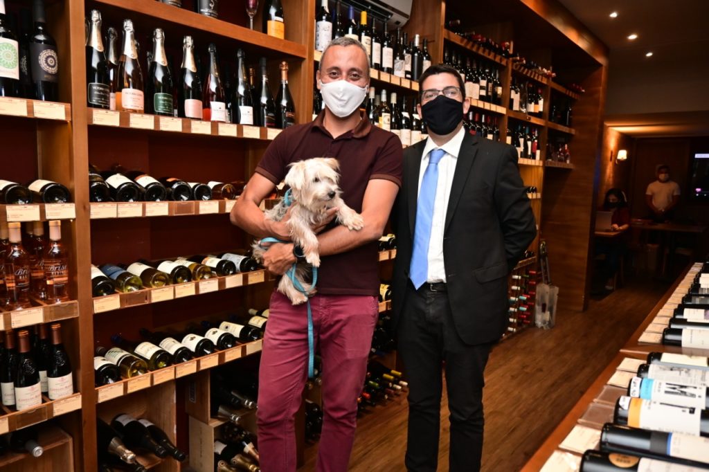 Imagem do Secretário de Agricultura Marcelo Queiroz com um cliente na loja de vinhos com um cachorro no colo